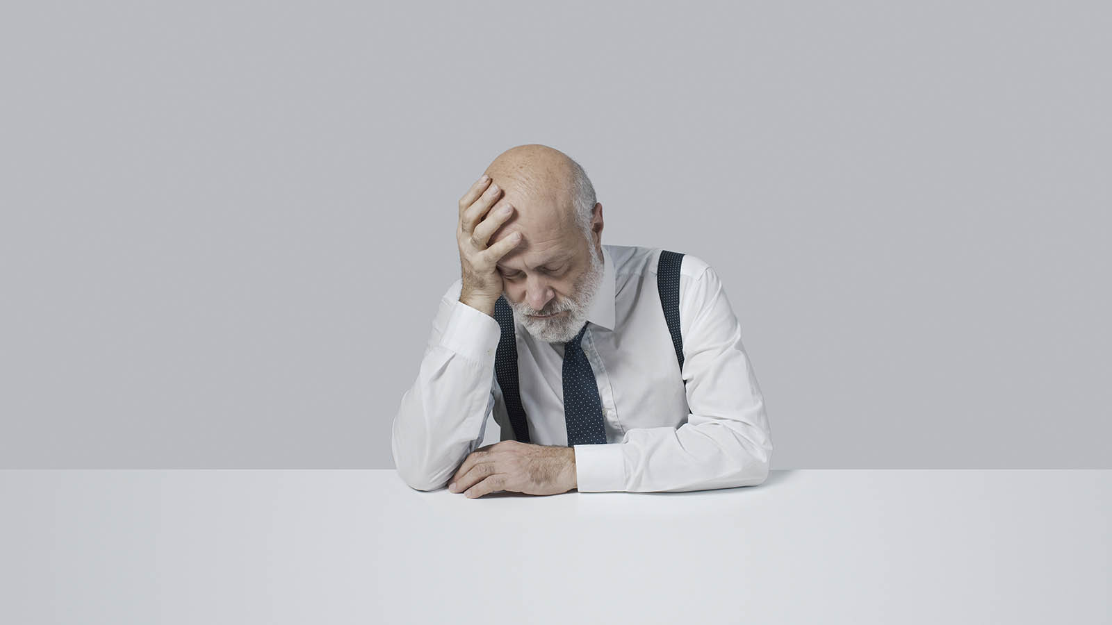 Senior man at table looking sad with head down